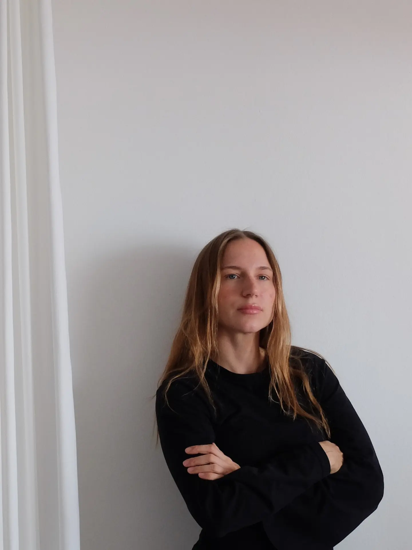 Anja Wittmann in einem schwarzen Longsleeve, Arme verschränkt, vor einer weißen Wand