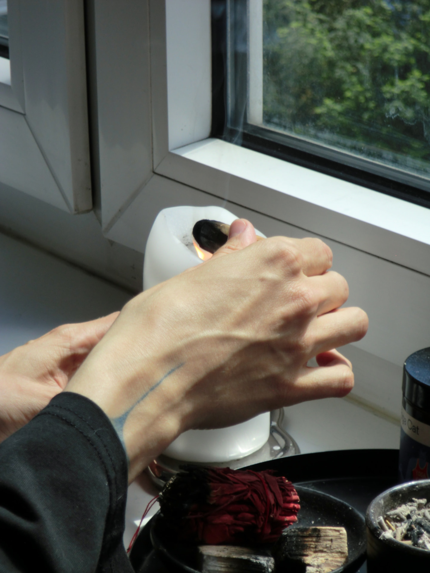 hands lighting palo santo on a sunlit windowsill